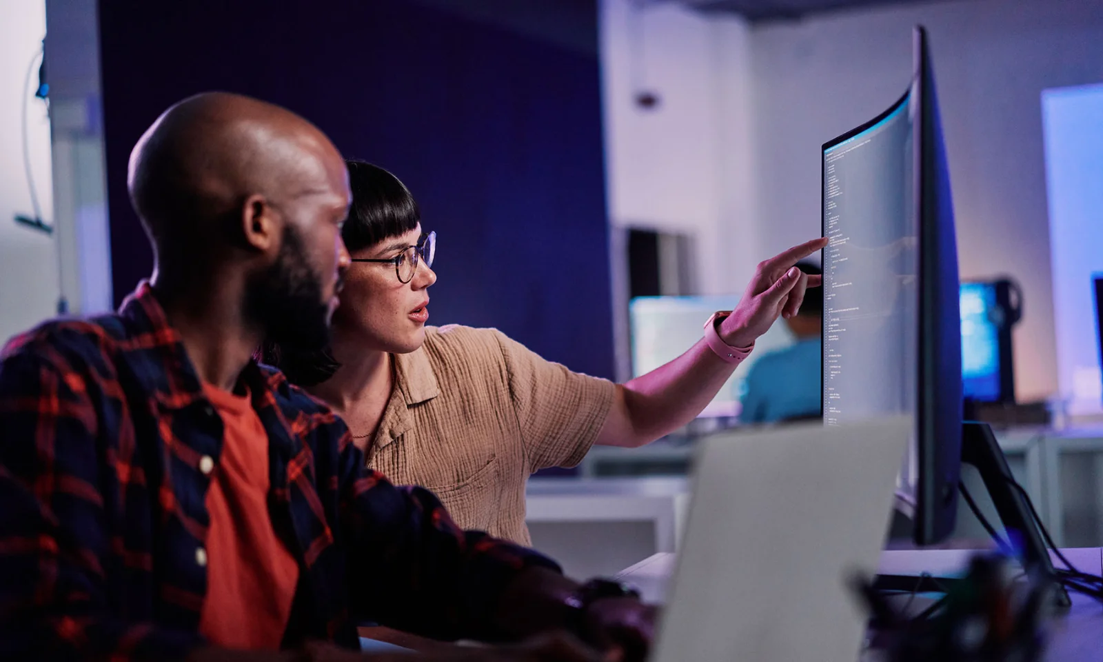 Code Review and Collaboration with Wynxx GenAI for Software Development Two developers reviewing code on a large monitor and discussing improvements while using Wynxx GenAI-powered software development tools