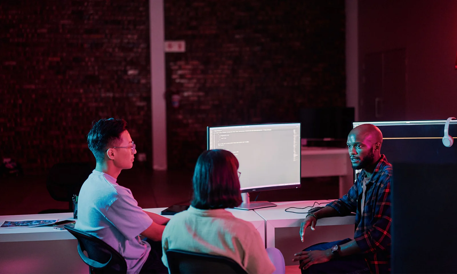 Three developers sitting at a workstation discussing code displayed on a monitor while using Wynxx GenAI-powered software development tools